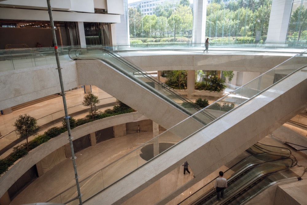 Modern retail podium atrium with escalators and a rooftop garden visible through glass, no text, no logos, no people