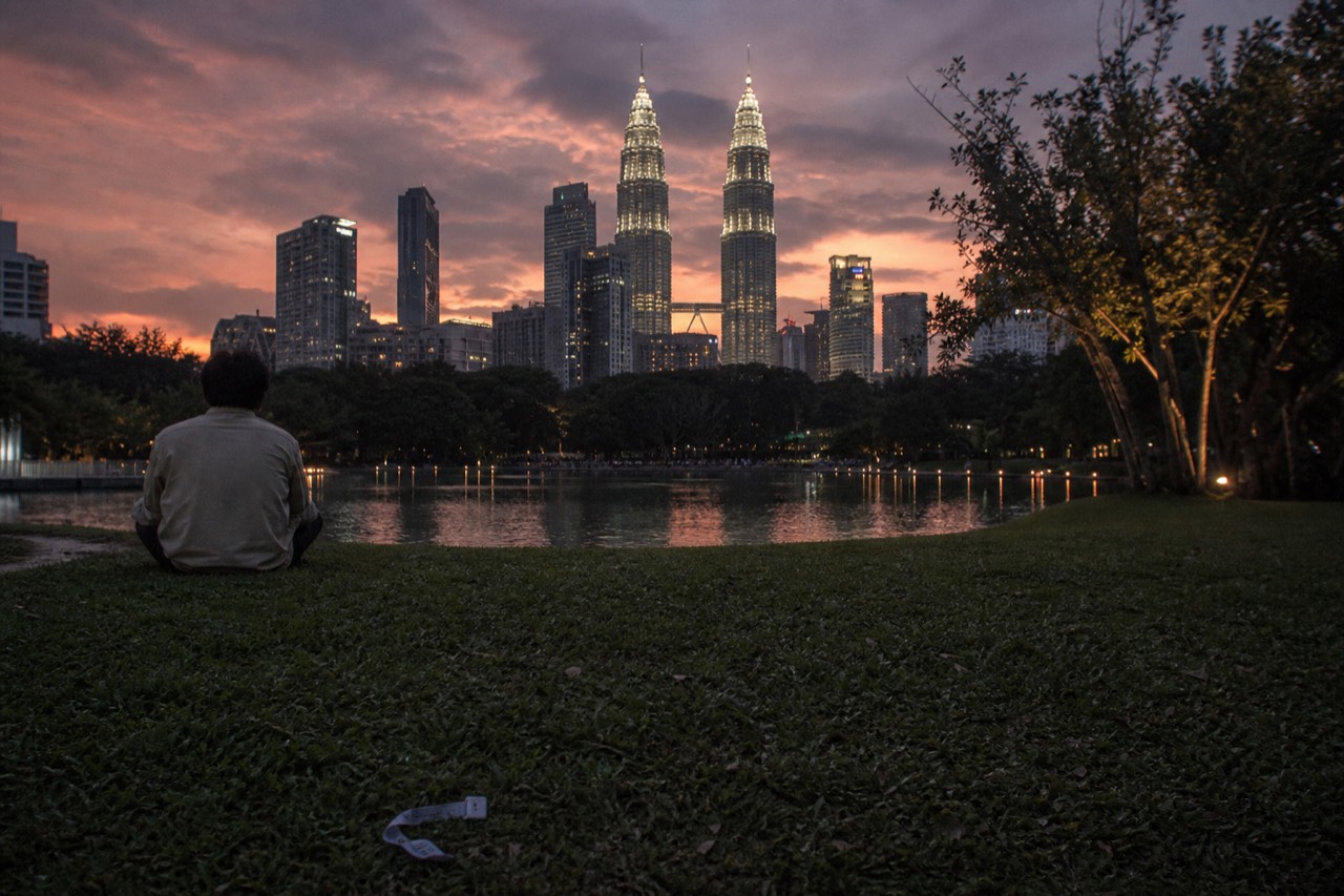Kuala Lumpur city skyline with the Petronas Twin Towers rising above the park at dusk, no text, no logos, no people