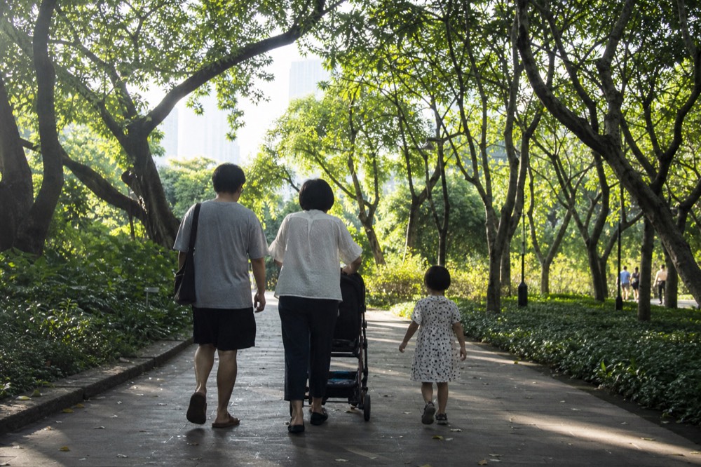 A family walking a stroller along a shaded park path near city towers, no text, no logos, no people