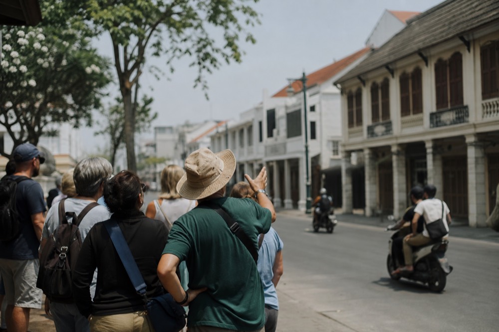 A walking tour group listening to a guide on a Kuala Lumpur street with colonial architecture behind, no text, no logos, no people