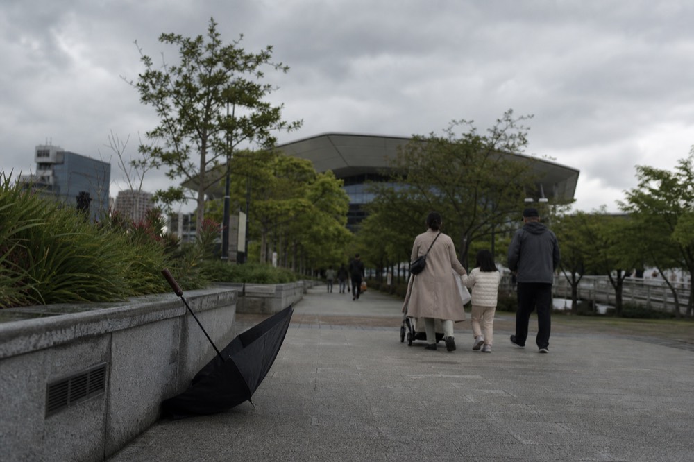 Visitors walking through KLCC Park toward the Convention Centre entrance as clouds gather, no text, no logos, no people
